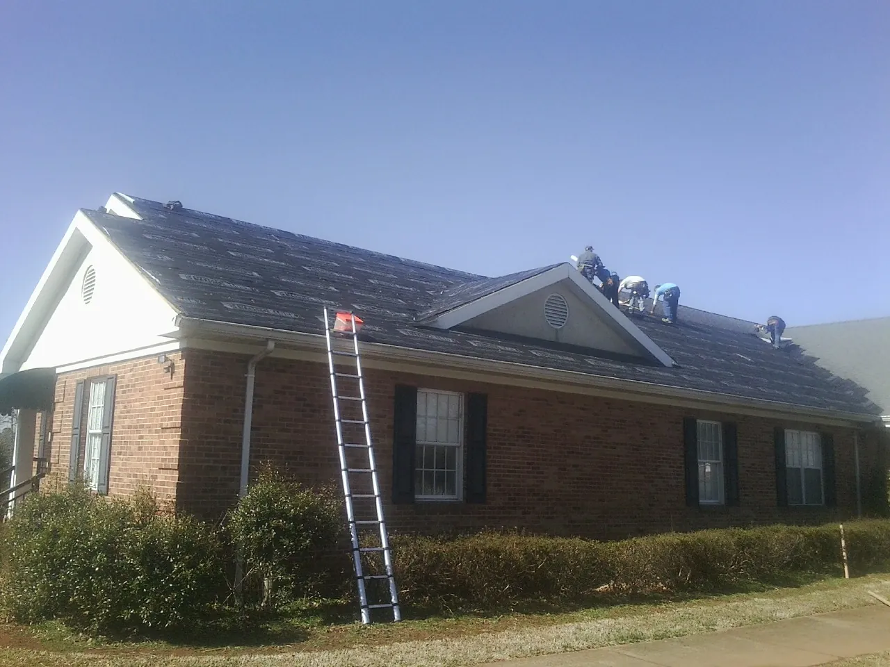Crew tearing shingles off a brick ranch roof with a ladder set — Metal Roof Repair work by our crew in Meridale