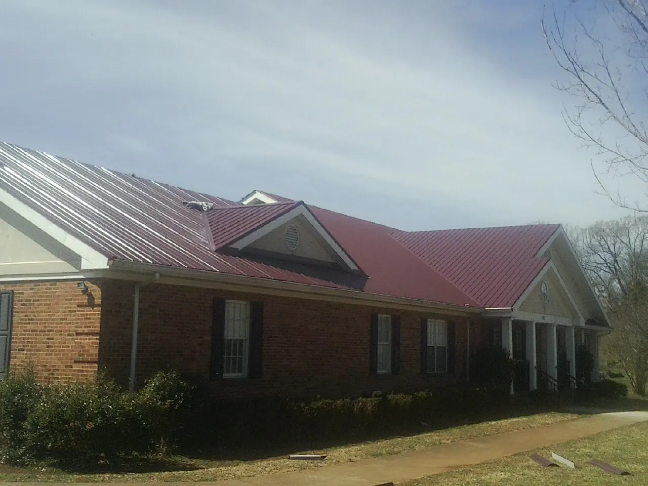 Red metal roof with gabled entries on a long brick building, from a Hail Damage Roof Repair job in Meridale