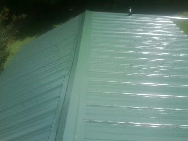 New green metal panels meeting at the ridge of a roof — Flat Roof Repair work by our crew in Meridale