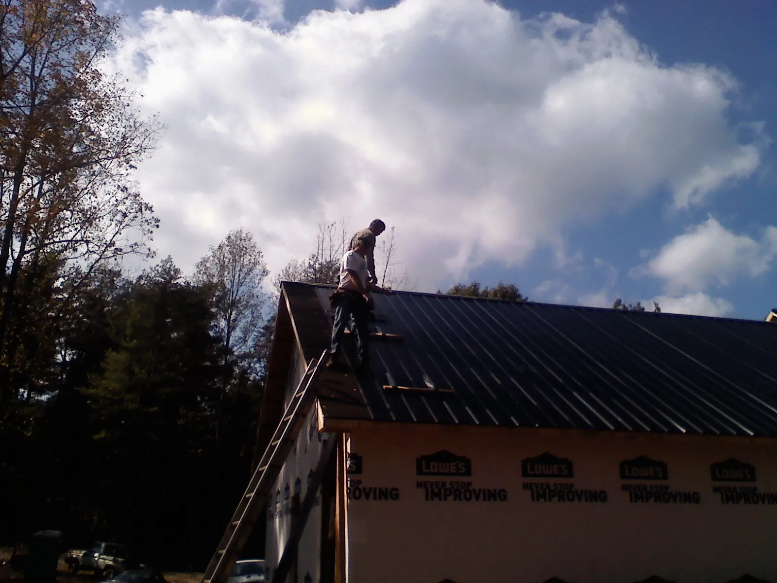 Roofer fastening dark metal panels high against a cloudy sky, from a Roof Inspection job in Meridale