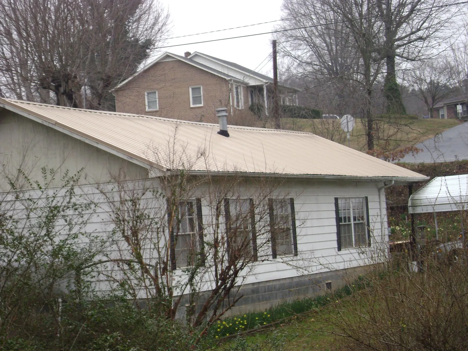 Tan metal roof on a white sided house set into a hillside — Commercial Roofing by Roofing Brothers in Meridale
